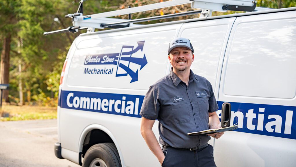 Smiling heating and cooling technician in front of Charles Stone commercial and residential van
