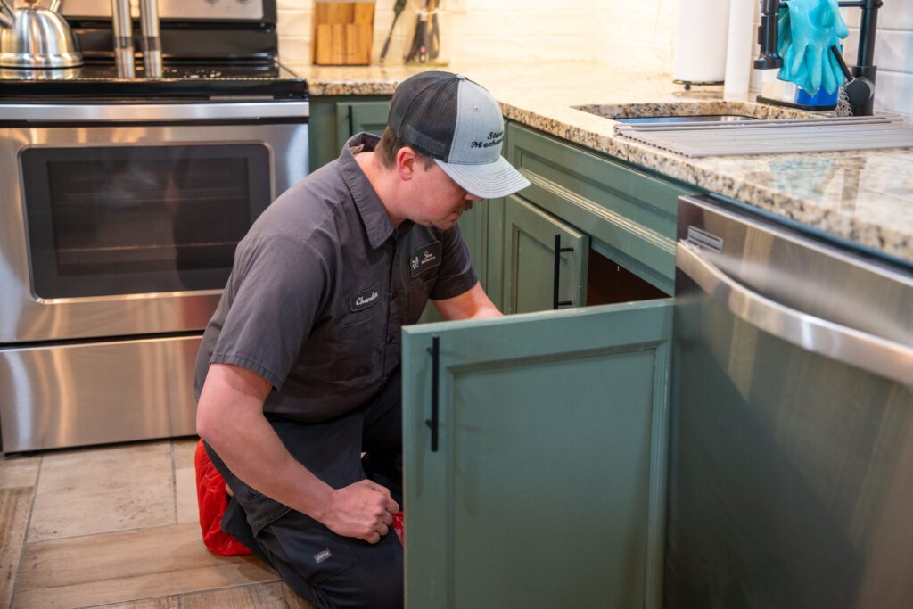 Plumbing technician inspecting pipes under kitchen sink