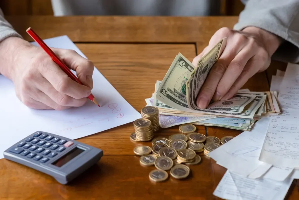 man at table writing down expenses and counting money, close-up of hands